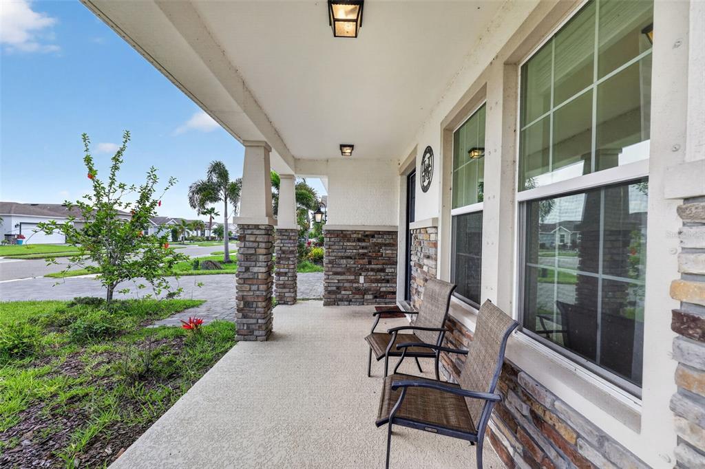 A covered front porch features stone-clad columns, a concrete floor, and two outdoor chairs — 6541 DEVESTA LOOP, PALMETTO, FL