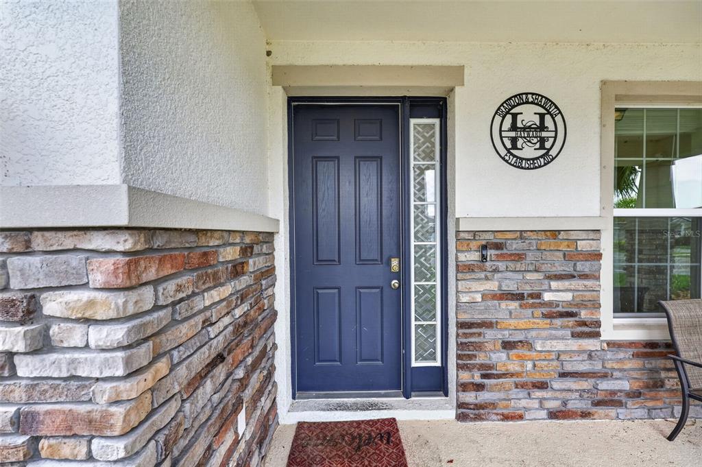 A blue front door with a side window is set in a stone-accented exterior wall — 6541 DEVESTA LOOP, PALMETTO, FL