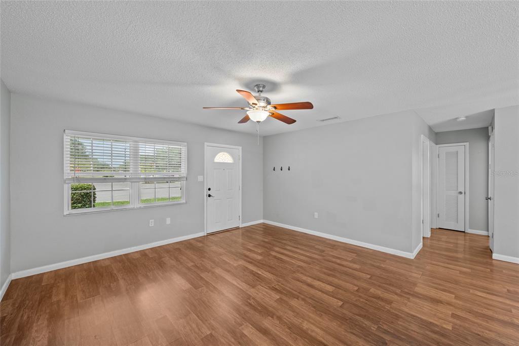 An empty room features light gray walls, wood-look flooring, a ceiling fan, and a front door — 3909 COLERIDGE PLACE, SARASOTA, FL