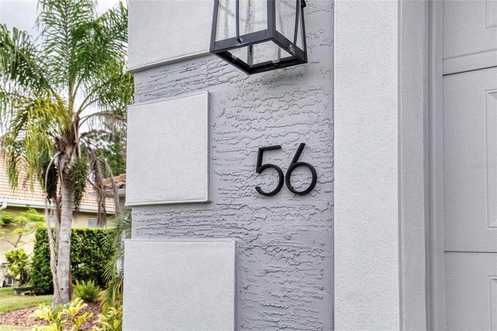 A close-up of a gray stucco exterior wall featuring the black house number 56 — 56 THORNHILL CHASE CIRCLE, ORMOND BEACH, FL