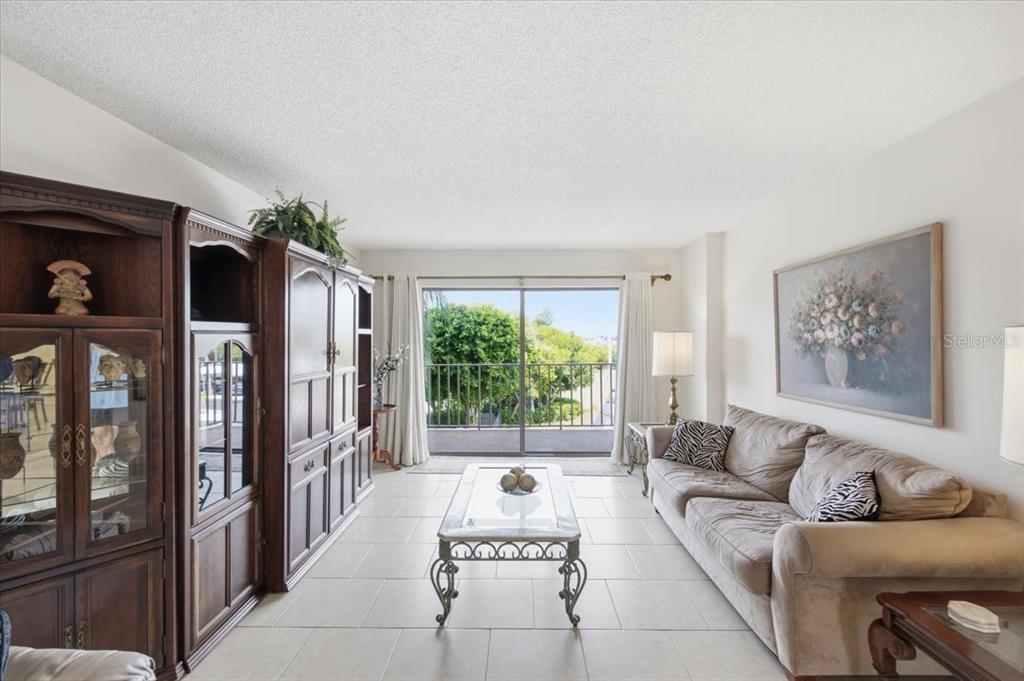 A living room features tile flooring, a large wooden entertainment center, and a sliding glass door — 7050 SUNSET DRIVE S UNIT 216, SOUTH PASADENA, FL