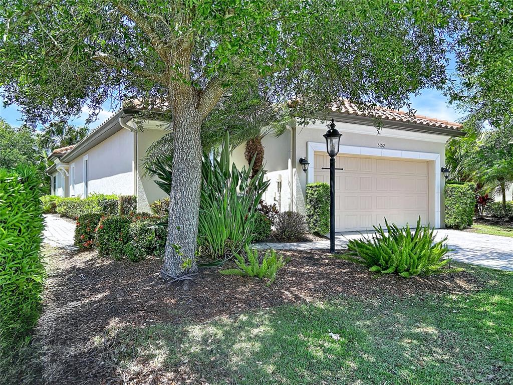 A single-story house with a beige garage, a tile roof, and landscaped front yard — 5102 SAVONA RUN, BRADENTON, FL