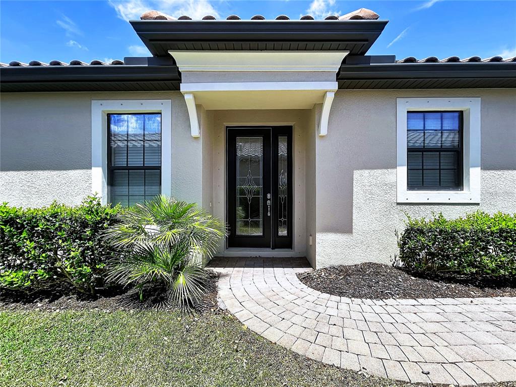 The front exterior of a house features a paved walkway leading to a dark door — 5102 SAVONA RUN, BRADENTON, FL