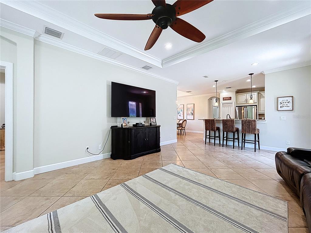 A living room with tile floors, a ceiling fan, a television console, and an open kitchen — 5102 SAVONA RUN, BRADENTON, FL