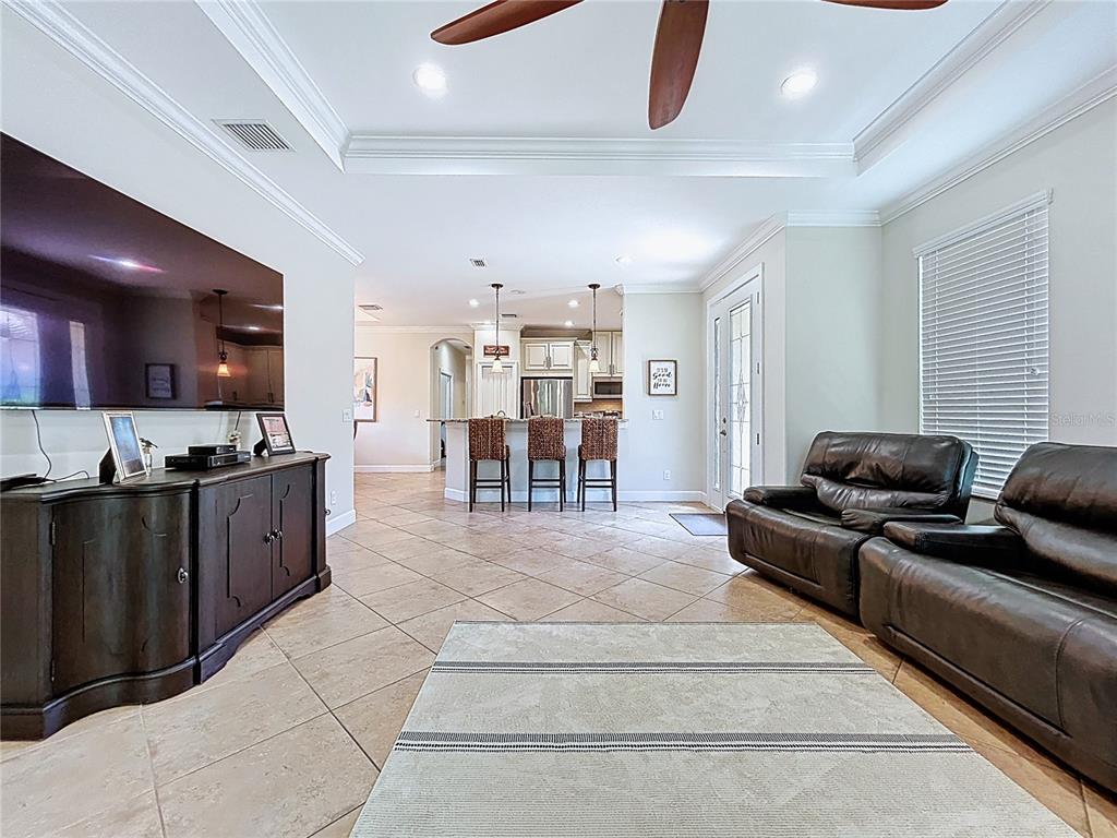 A living room with tile floors, a large television, and an open kitchen with bar seating — 5102 SAVONA RUN, BRADENTON, FL
