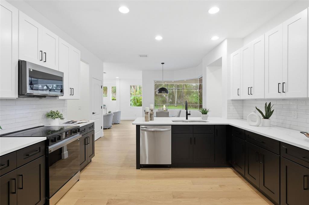 A modern kitchen features white upper cabinets, dark lower cabinets, and light wood flooring — 10534 BERMUDA ISLE DRIVE, TAMPA, FL