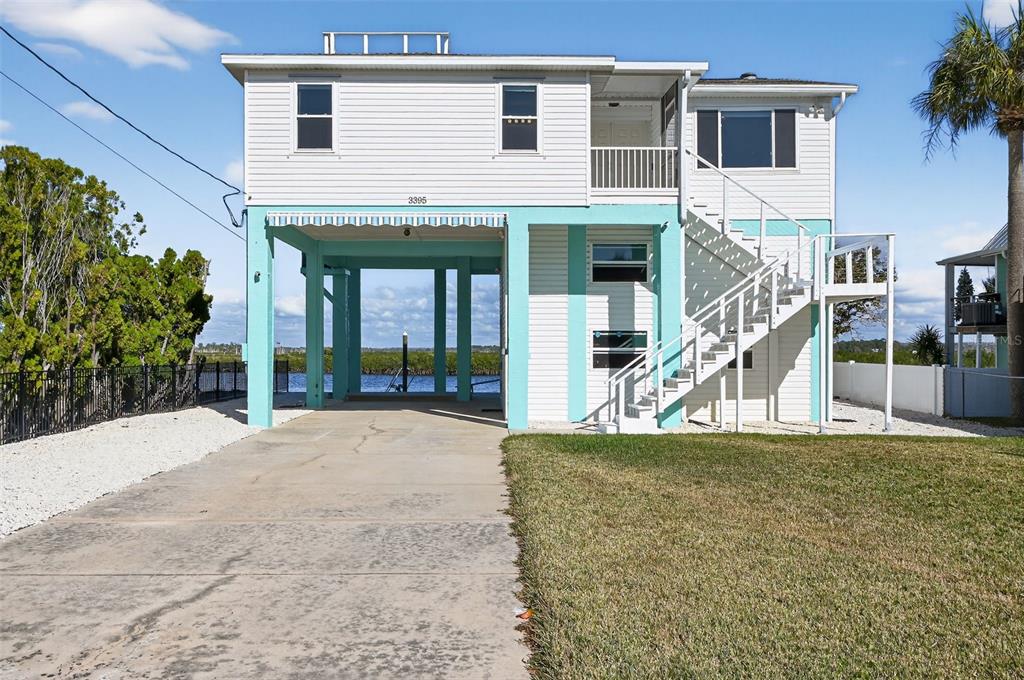A two-story coastal home on stilts features a concrete driveway, exterior stairs, and turquoise accents — 3395 EAGLE NEST DRIVE, HERNANDO BEACH, FL