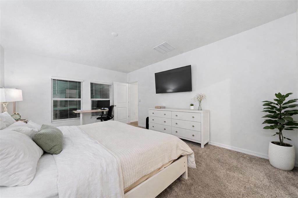 A bedroom features a bed, a white dresser with a wall-mounted television, and a desk — 3977 WILLOWBROOK DRIVE, EDGEWATER, FL