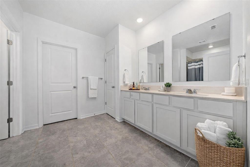 A bathroom features a double vanity with light gray cabinets, large mirrors, and tile flooring — 3977 WILLOWBROOK DRIVE, EDGEWATER, FL