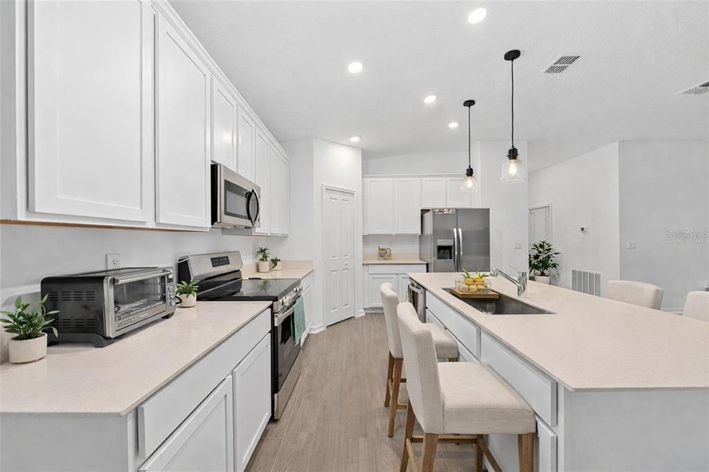 A modern kitchen features white cabinets, stainless steel appliances, and a large central island — 3977 WILLOWBROOK DRIVE, EDGEWATER, FL