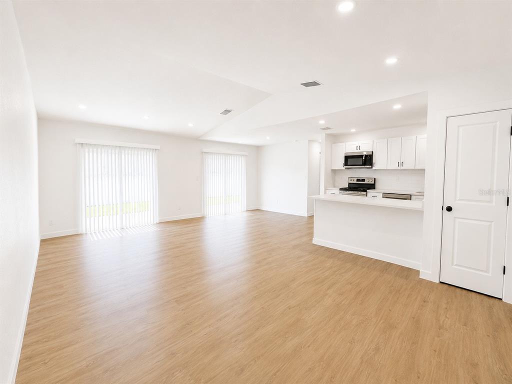 An open-concept living area with light wood-look flooring and a white kitchen with stainless appliances — 3386 39TH STREET S UNIT B, ST PETERSBURG, FL