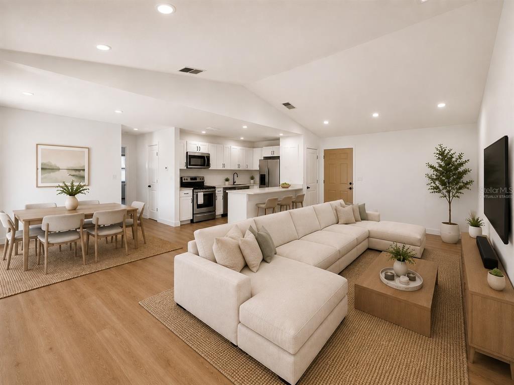 An open-concept living room and kitchen with light wood floors and a large sectional sofa — 3386 39TH STREET S UNIT B, ST PETERSBURG, FL