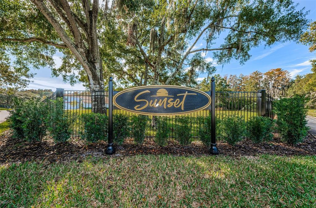 A black metal fence surrounds a grassy area with a sign reading Sunset — 4445 LANSBROOK PARKWAY, PALM HARBOR, FL