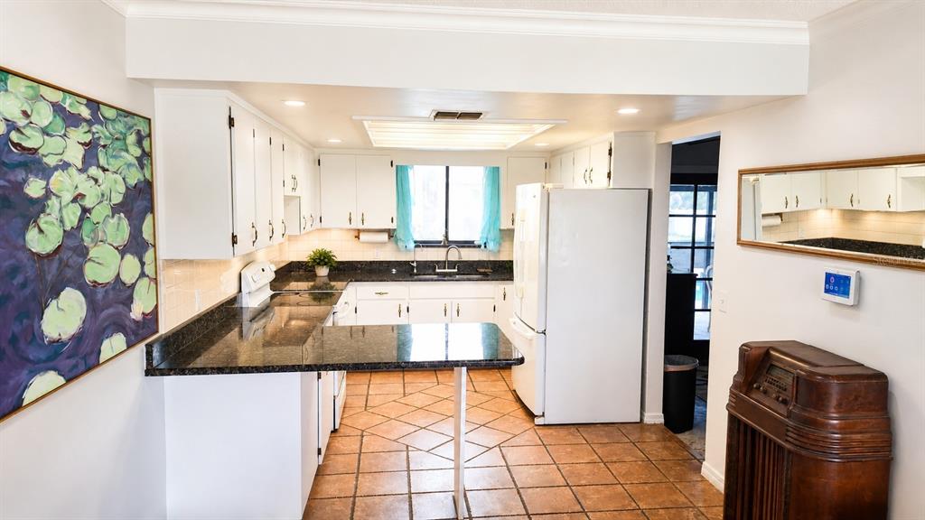 A kitchen features white cabinets, dark granite countertops, tile flooring, and a large wall painting — 2234 W MAPLE TERRACE, ST CLOUD, FL
