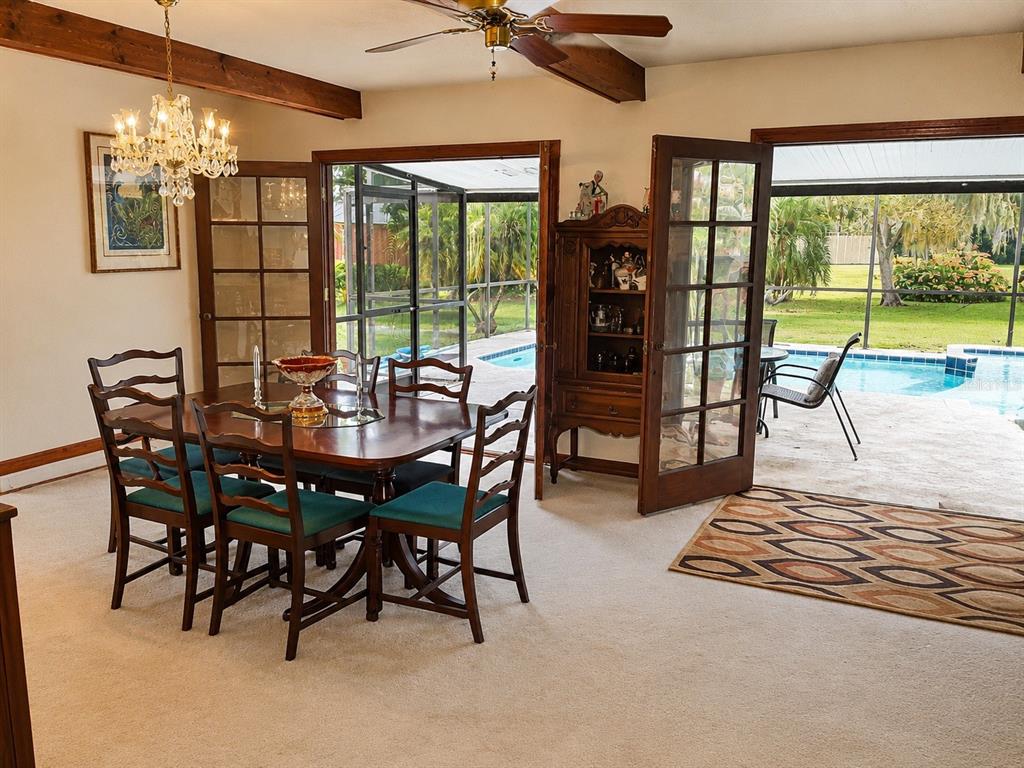 A dining room with a wooden table, chandelier, and French doors opening to a pool patio — 2234 W MAPLE TERRACE, ST CLOUD, FL