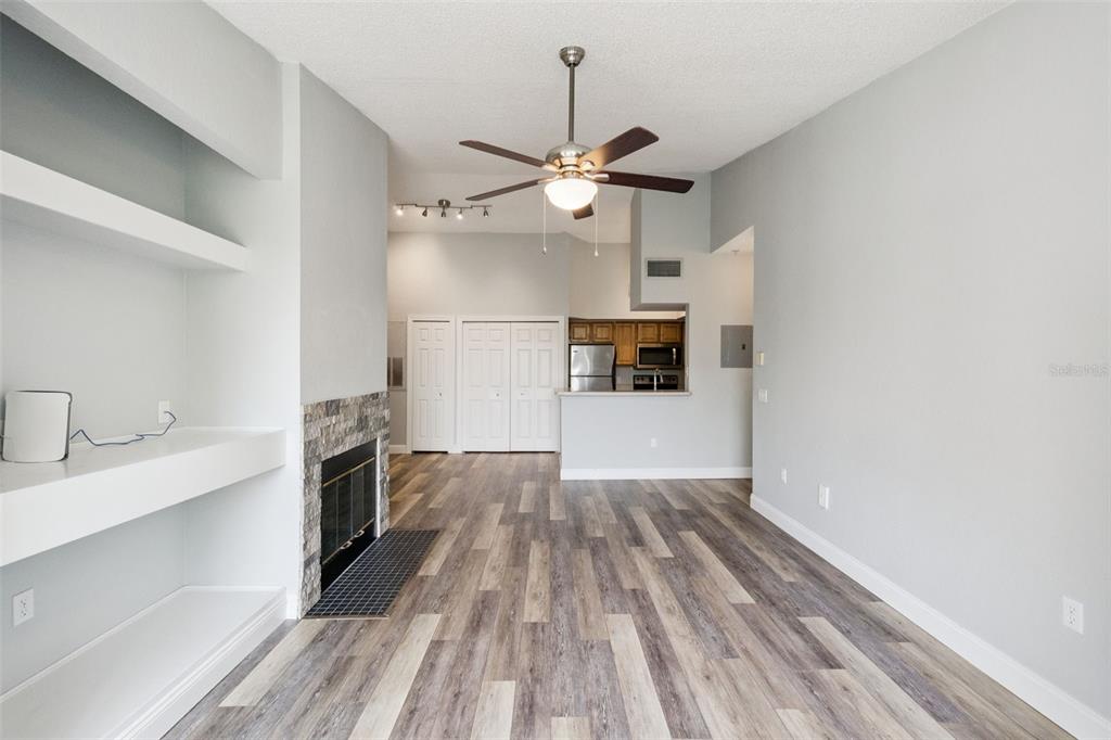 A living room with wood-look flooring, a stone fireplace, built-in shelving, and an open kitchen — 13015 PLANTATION PARK CIRCLE UNIT 1035, ORLANDO, FL