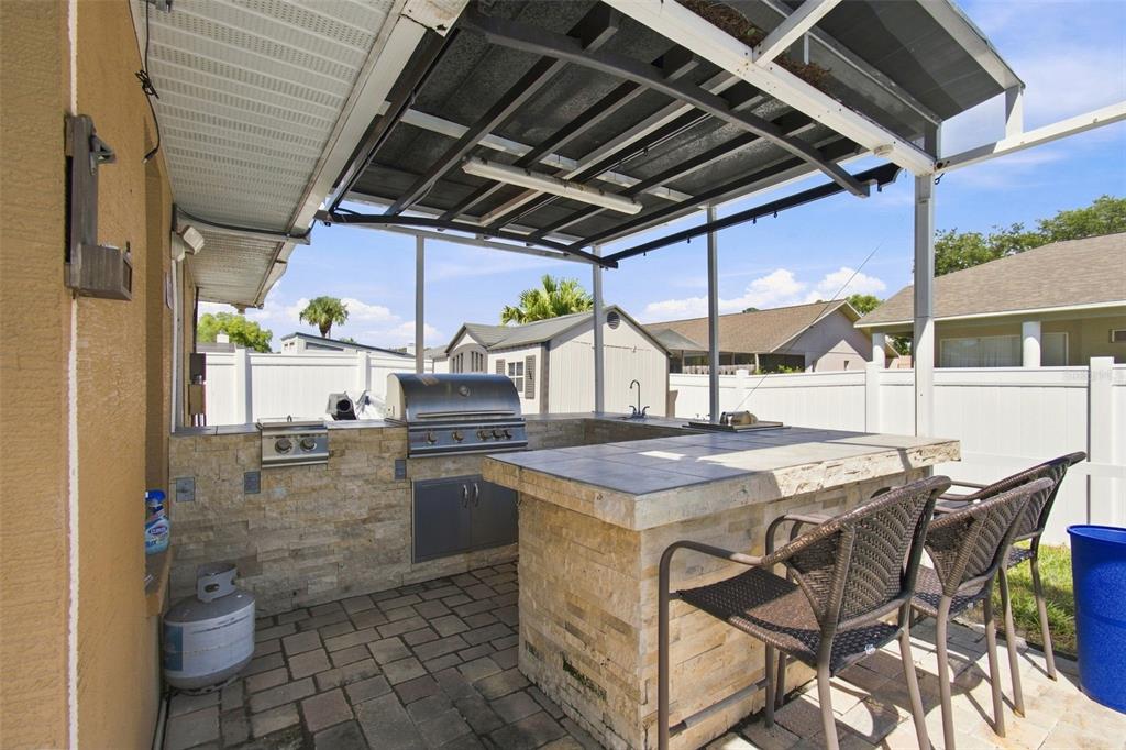 An outdoor kitchen with a stone-faced bar, grill, and covered patio area in a backyard — 10149 BRIAR CIRCLE, HUDSON, FL