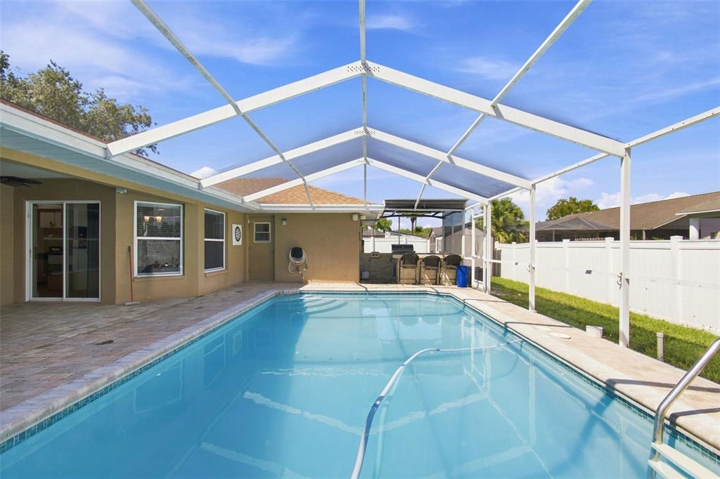 A swimming pool with a screened enclosure sits on a patio next to a house — 10149 BRIAR CIRCLE, HUDSON, FL