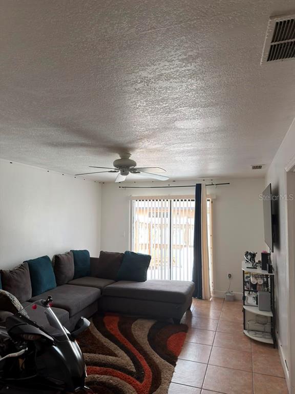 A living room features a sectional sofa, a patterned rug, tile flooring, and a ceiling fan — 2207 CARIBBEAN DRIVE, KISSIMMEE, FL