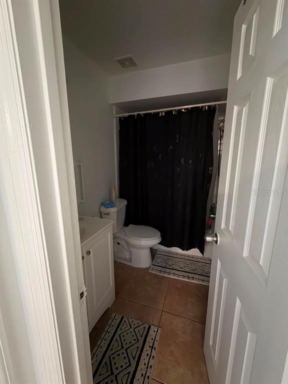 A small bathroom features a white vanity, a toilet, and a shower with a black curtain — 2207 CARIBBEAN DRIVE, KISSIMMEE, FL