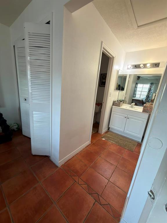 A hallway with terracotta tile flooring leads to a bathroom vanity and a closet — 2207 CARIBBEAN DRIVE, KISSIMMEE, FL