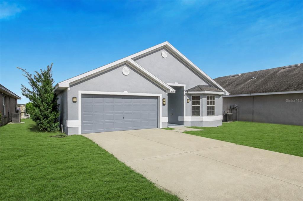 A gray single-story house features a two-car garage, a bay window, and a concrete driveway — 4099 ISLAND LAKES DRIVE, WINTER HAVEN, FL