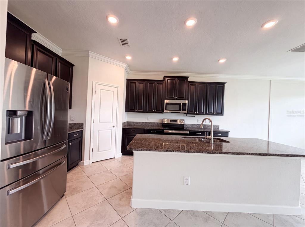 A kitchen features dark wood cabinets, granite countertops, stainless steel appliances, and tile flooring — 9709 IVORY DRIVE, RUSKIN, FL