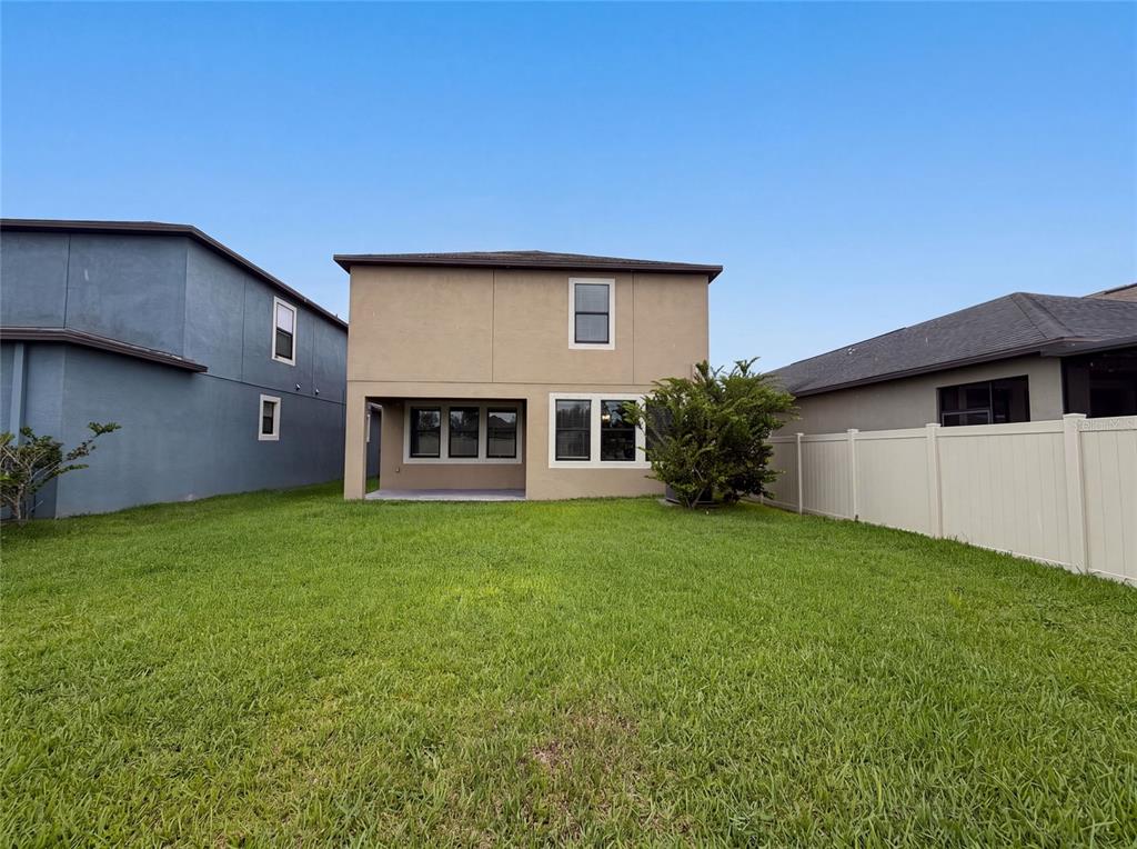 The rear exterior of a two-story beige house features a small patio and lawn — 9709 IVORY DRIVE, RUSKIN, FL