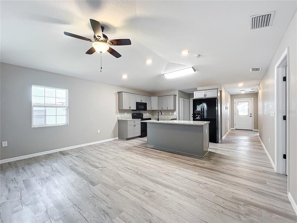 An open-concept kitchen and living area features light gray flooring, gray cabinetry, and a kitchen island — 7091 TAMARIND WAY, LAKE WALES, FL