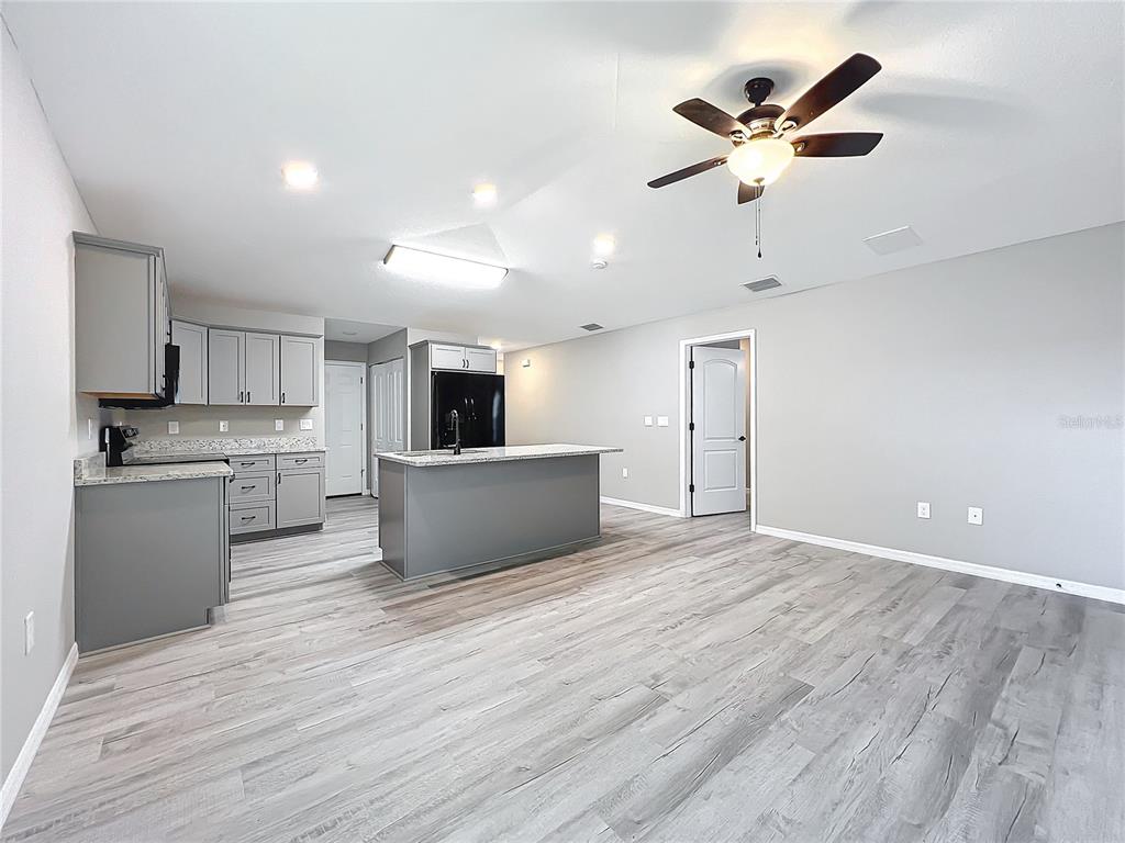 A kitchen with grey cabinets and a central island opens into a spacious living area — 7091 TAMARIND WAY, LAKE WALES, FL