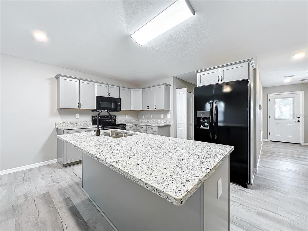 A kitchen features gray cabinets, speckled granite countertops, a central island, and black appliances — 7091 TAMARIND WAY, LAKE WALES, FL