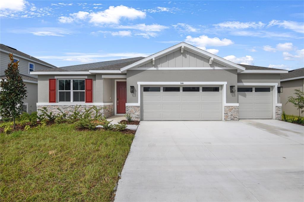 A single-story house features a gray stucco exterior, stone veneer accents, and a red front door — 1666 CROOKED CREEK STREET, ST CLOUD, FL