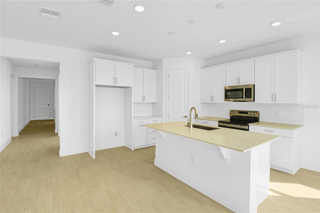 A modern kitchen features white cabinetry, a central island with a sink, and light-colored flooring — 1666 CROOKED CREEK STREET, ST CLOUD, FL
