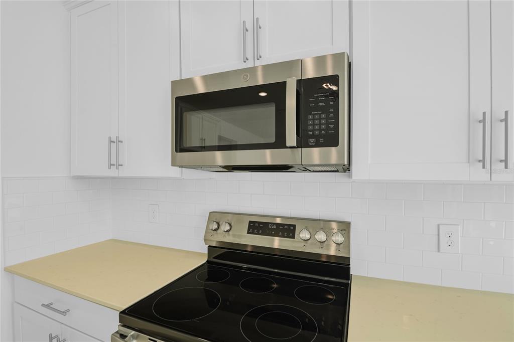 A kitchen features white cabinets, a stainless steel microwave, and a black electric range — 1666 CROOKED CREEK STREET, ST CLOUD, FL