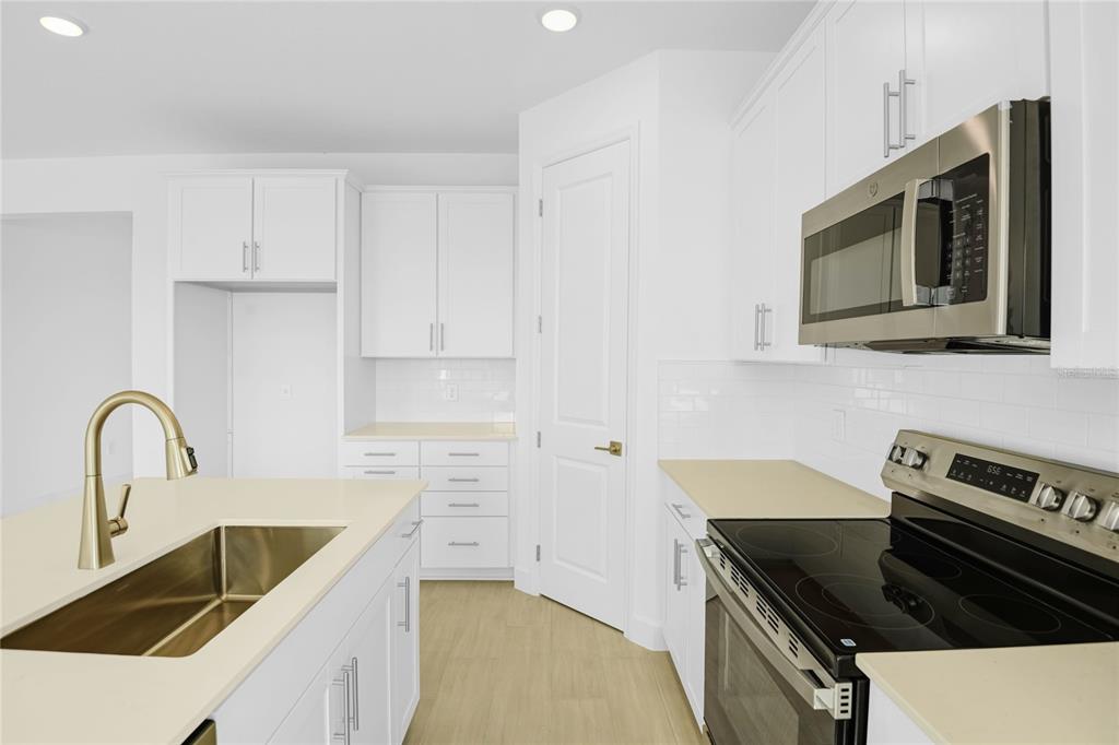 A modern kitchen features white cabinets, stainless steel appliances, a kitchen island, and light flooring — 1666 CROOKED CREEK STREET, ST CLOUD, FL