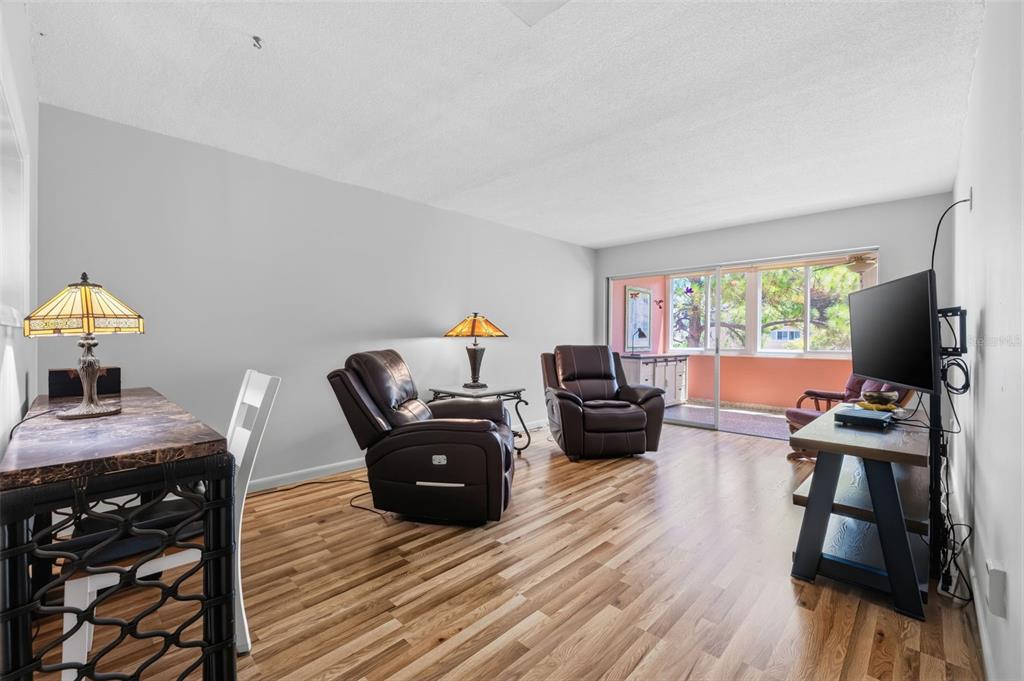 A living room with wood-look flooring, two leather recliners, a desk, and a sliding glass door — 9940 47TH AVENUE N UNIT 216, ST PETERSBURG, FL