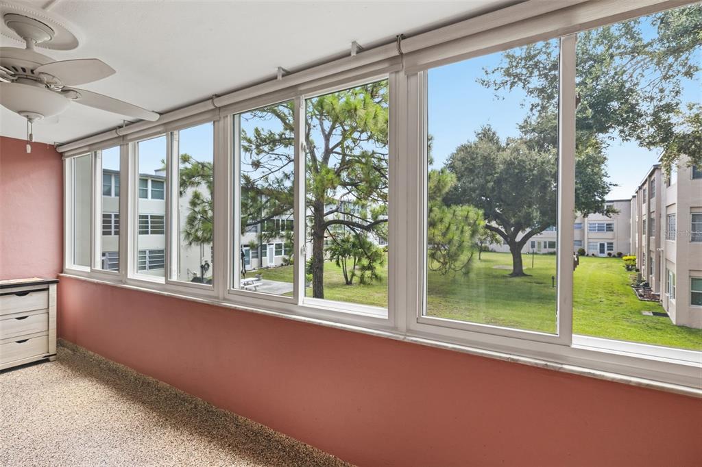 A sunroom with pink walls, a ceiling fan, and large windows overlooking a grassy courtyard — 9940 47TH AVENUE N UNIT 216, ST PETERSBURG, FL