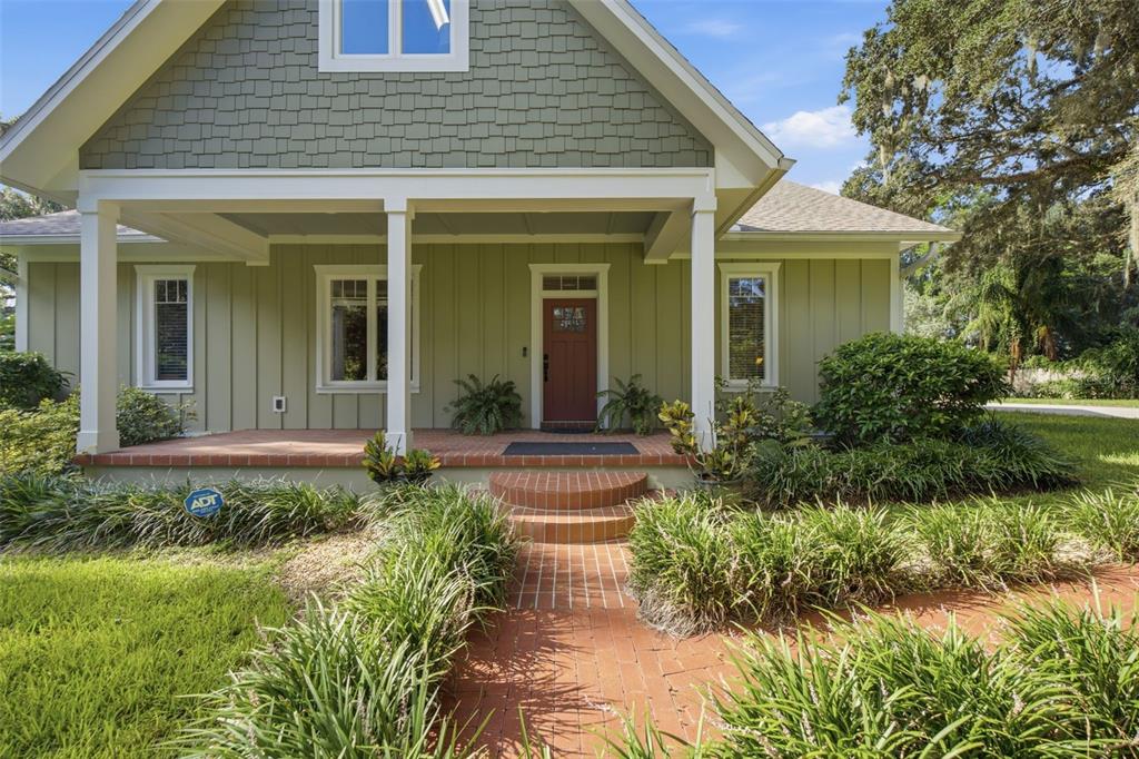 A green house with a brick porch and walkway, white columns, and a red front door — 1905 PINE STREET, VALRICO, FL