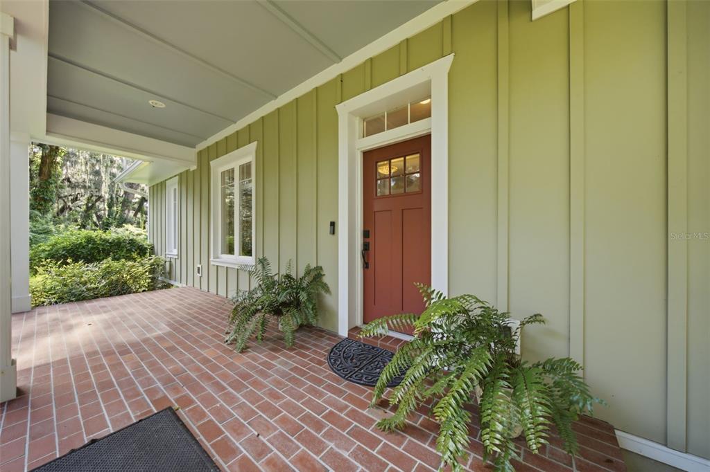 A covered brick porch features a red front door, board-and-batten siding, and potted ferns — 1905 PINE STREET, VALRICO, FL