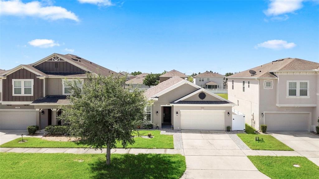 A street-level view of three suburban houses with driveways and lawns under a blue sky — 2050 BEACON LANDING CIRCLE, ORLANDO, FL