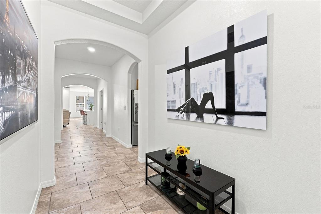 A hallway with tile flooring, arched doorways, and wall art leads toward a kitchen area — 2050 BEACON LANDING CIRCLE, ORLANDO, FL