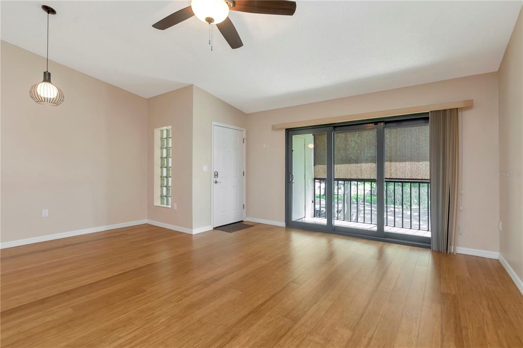 An empty living room features light wood flooring, a ceiling fan, and a sliding glass door — 3367 CRYSTAL COURT E UNIT E, PALM HARBOR, FL