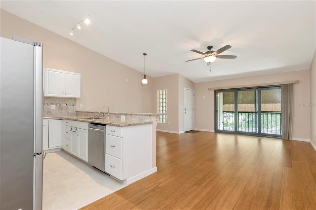 A kitchen with white cabinets and granite counters opens to a living area with flooring — 3367 CRYSTAL COURT E UNIT E, PALM HARBOR, FL