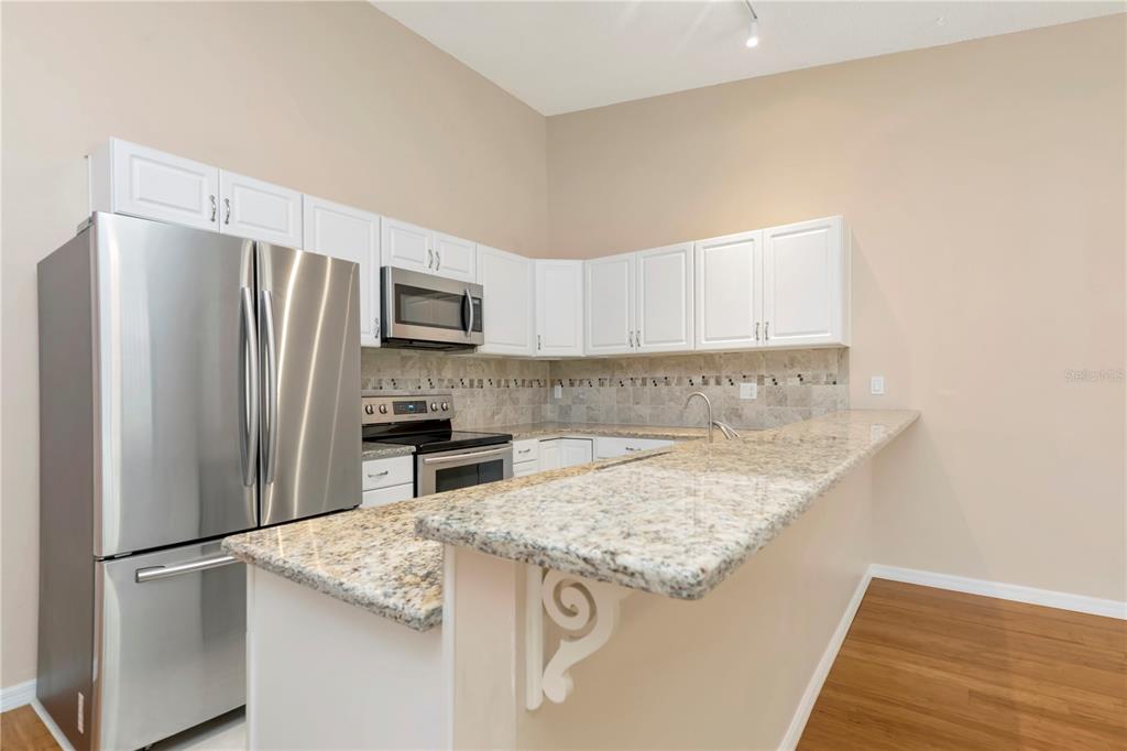 A kitchen features white cabinets, granite countertops, stainless steel appliances, and a breakfast bar — 3367 CRYSTAL COURT E UNIT E, PALM HARBOR, FL