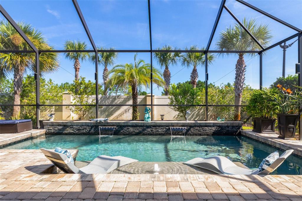A screened-in swimming pool features two lounge chairs on a tanning ledge and water features — 2 DEL PALMA DRIVE, PALM COAST, FL