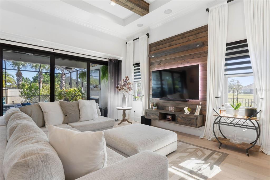 A living room features a wood-paneled accent wall with a mounted television and sliding glass doors — 2 DEL PALMA DRIVE, PALM COAST, FL