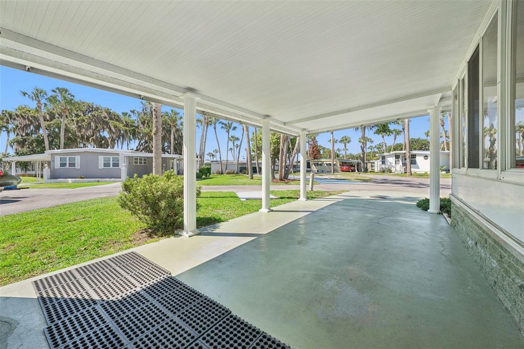 A covered concrete carport with white support columns overlooks a grassy neighborhood with palm trees — 43 SABAL PALM CIRCLE, EUSTIS, FL