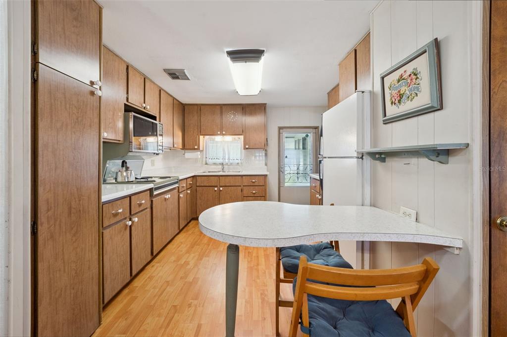A kitchen features wood cabinets, a white countertop, a breakfast bar, and light wood flooring — 43 SABAL PALM CIRCLE, EUSTIS, FL