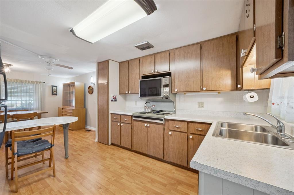 A kitchen features wood cabinets, white countertops, a stainless steel sink, and a dining area — 43 SABAL PALM CIRCLE, EUSTIS, FL