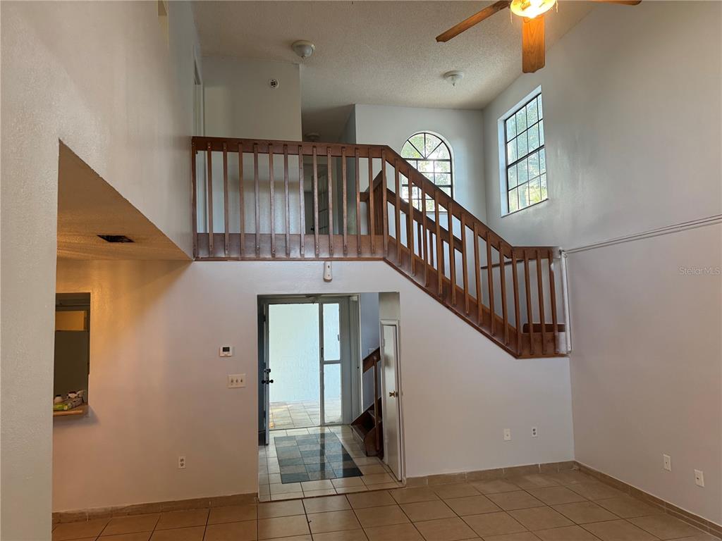 A high-ceilinged room features tile flooring, a wooden staircase with a railing, and an entryway — 1212 INDIAN BLUFF DRIVE, APOPKA, FL